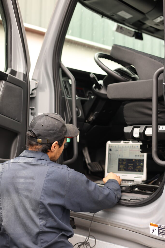 Technician using diagnostic equipment beside a semi-truck cab